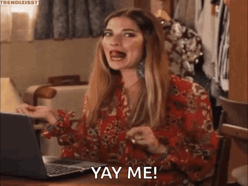 A Woman In A Red Dress Is Sitting At A Table With A Laptop And Making A Funny Face . GIF