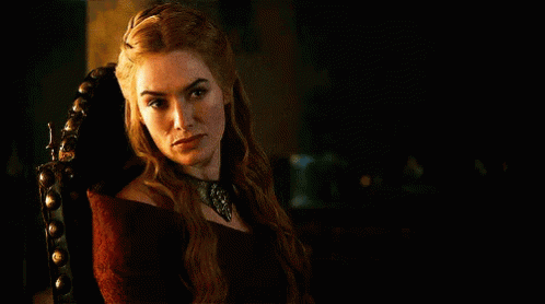 A Woman In A Red Dress Is Sitting In A Chair In A Dark Room And Looking At The Camera . GIF