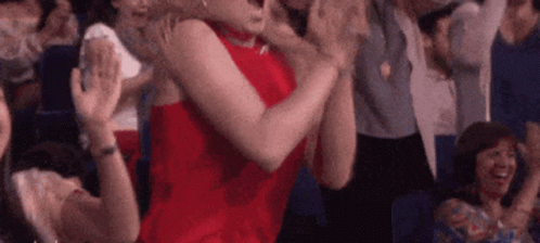 A Woman In A Red Dress Is Sitting In A Crowd Of People Clapping Their Hands . GIF