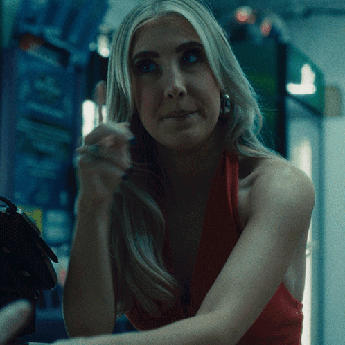 A Woman In A Red Dress Is Sitting In A Dark Room GIF