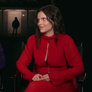 A Woman In A Red Dress Is Sitting In Front Of A Door GIF
