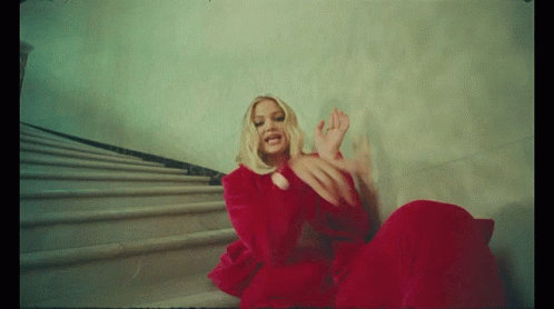 A Woman In A Red Dress Is Sitting On Some Stairs GIF