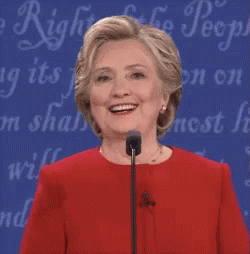 A Woman In A Red Dress Is Smiling In Front Of A Sign That Says ' Freedom Of The People ' GIF