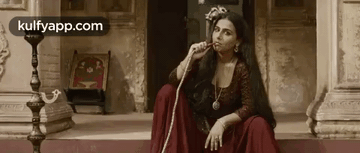A Woman In A Red Dress Is Smoking A Hookah While Sitting On The Steps Of A Building . GIF