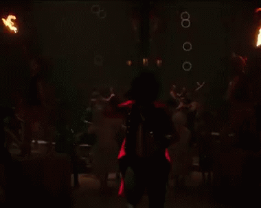 A Woman In A Red Dress Is Spinning A Hula Hoop With Fireworks Behind Her GIF