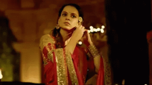 A Woman In A Red Dress Is Standing In A Dark Room Holding A Flower In Her Hand . GIF