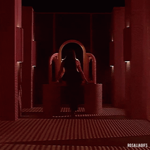 A Woman In A Red Dress Is Standing In A Dark Room With A Red Light Behind Her . GIF