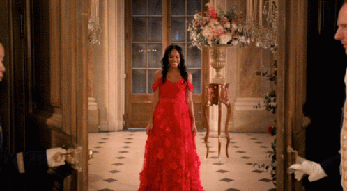 A Woman In A Red Dress Is Standing In A Doorway GIF