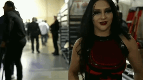A Woman In A Red Dress Is Standing In A Hallway With People Walking Behind Her . GIF