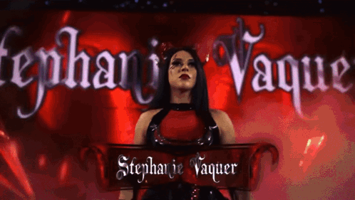 A Woman In A Red Dress Is Standing In Front Of A Banner That Says Stephanie Vaquer GIF