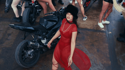A Woman In A Red Dress Is Standing In Front Of A Black Motorcycle GIF