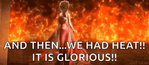 A Woman In A Red Dress Is Standing In Front Of A Fire With The Words And Then We Had Heat ! It Is Glorious ! GIF