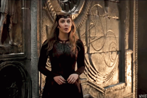 A Woman In A Red Dress Is Standing In Front Of A Stone Wall With The Letters Wwe On The Bottom Right GIF