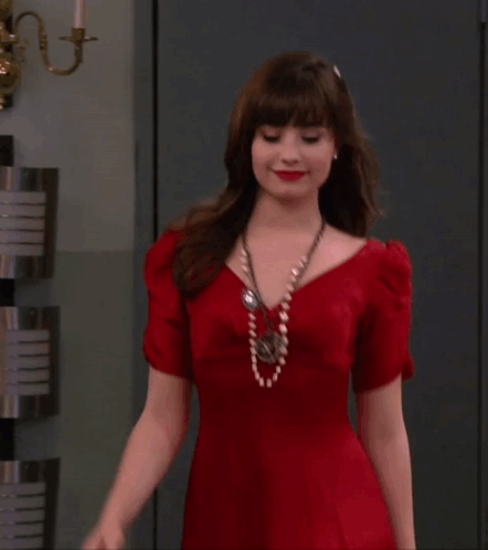 A Woman In A Red Dress Is Standing In Front Of A Wall GIF