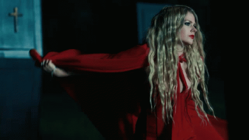 A Woman In A Red Dress Is Standing In Front Of A Wall With A Cross On It GIF