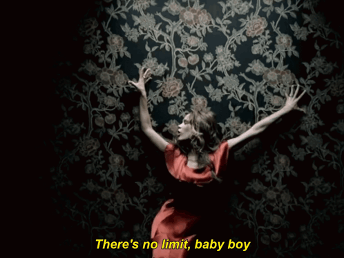 A Woman In A Red Dress Is Standing In Front Of A Wall With Flowers And The Words There 'S No Limit GIF