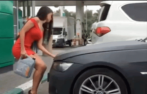 A Woman In A Red Dress Is Standing Next To A Car Holding A Gallon Of Oil GIF