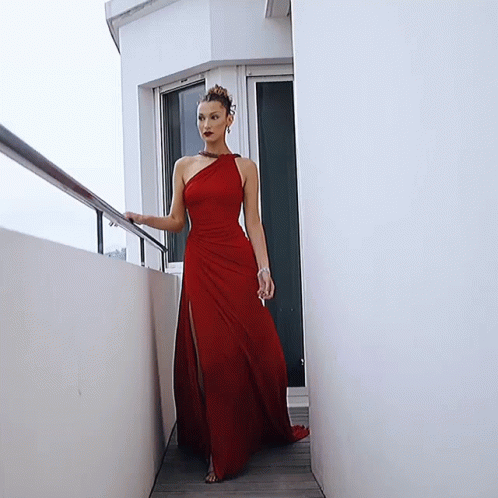 A Woman In A Red Dress Is Standing Next To A White Wall GIF