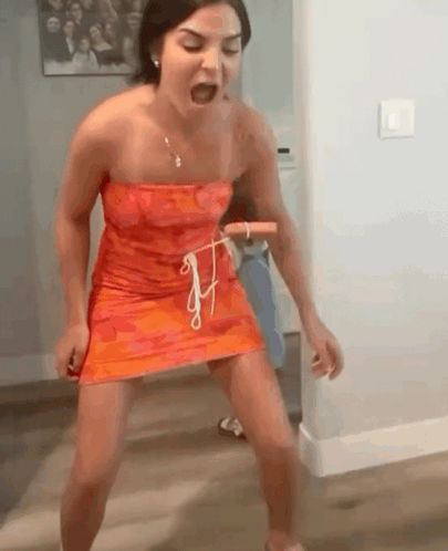 A Woman In A Red Dress Is Standing On A Wooden Floor Holding A Rope . GIF