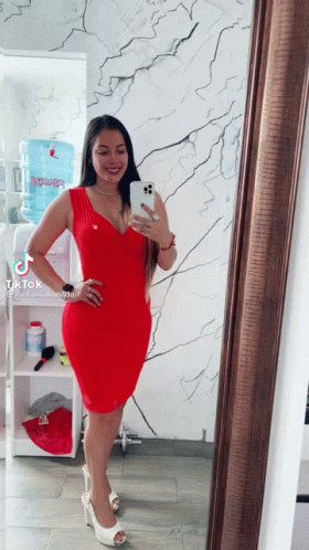 A Woman In A Red Dress Is Taking A Picture Of Herself In Front Of A Mirror GIF