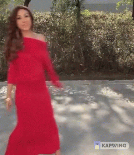 A Woman In A Red Dress Is Walking Down A Road . GIF