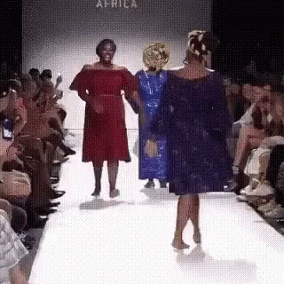 A Woman In A Red Dress Is Walking Down A Runway At A Fashion Show . GIF