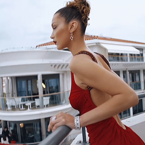 A Woman In A Red Dress Leans On A Railing GIF