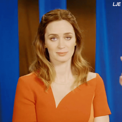 A Woman In A Red Dress Stands In Front Of A Blue Curtain With The Letters Lje On The Bottom Right GIF