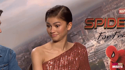 A Woman In A Red Dress Stands In Front Of A Poster That Says Spider-Man Far From Home GIF