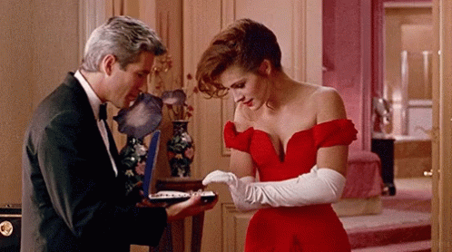 A Woman In A Red Dress Stands Next To A Man In A Black Suit GIF