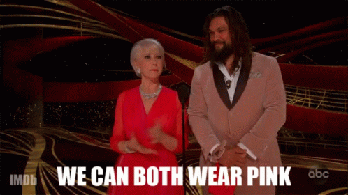 A Woman In A Red Dress Stands Next To A Man In A Pink Suit With The Words We Can Both Wear Pink Behind Them GIF