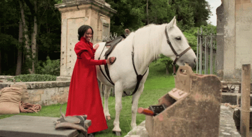 A Woman In A Red Dress Stands Next To A White Horse GIF