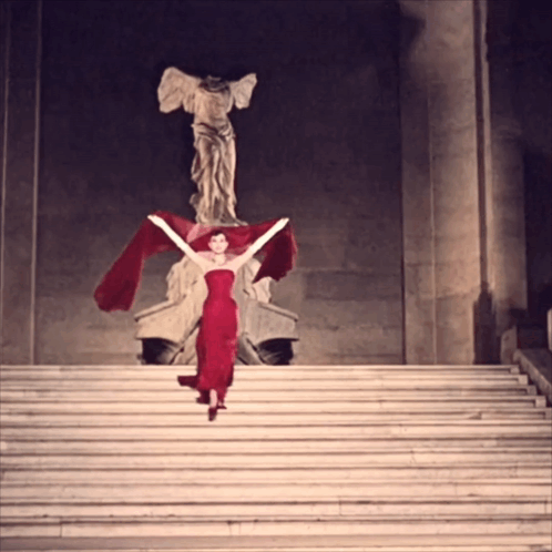 Woman In Red Dress On Stairs In Front Of Statue GIF