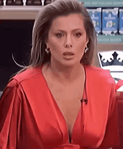 A Woman In A Red Dress With A Plunging Neckline Is Talking On A Microphone . GIF