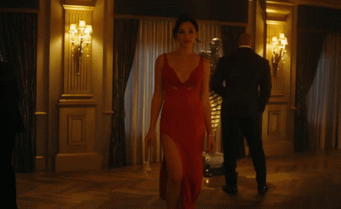 A Woman In A Red Dress With A Plunging Neckline Is Walking In A Room GIF