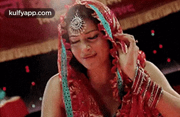 A Woman In A Red Dress With A Veil On Her Head Is Looking Down . GIF