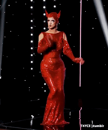 A Woman In A Red Dress With Horns On Her Head Is Standing On A Stage . GIF