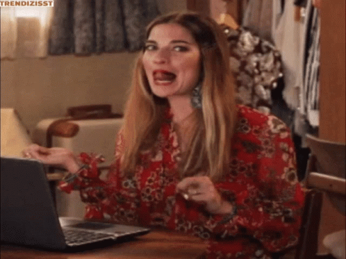 A Woman In A Red Floral Shirt Is Sitting At A Table With A Laptop . GIF
