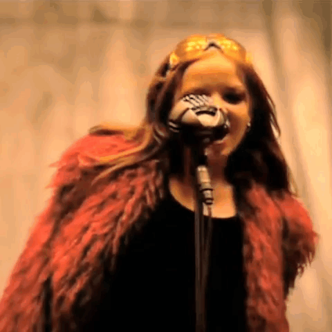 A Woman In A Red Fur Coat Singing Into A Microphone . GIF