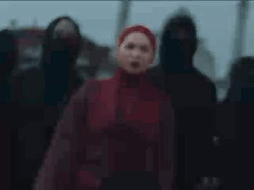 A Woman In A Red Hijab Is Standing In Front Of A Group Of People In Black Hoods . GIF