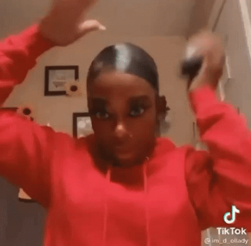 A Woman In A Red Hoodie Is Holding Her Hair Up In A Bun . GIF