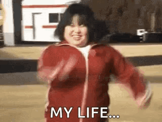 A Woman In A Red Jacket Is Dancing And Smiling While Saying `` My Life ... '' . GIF