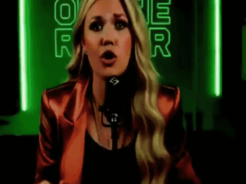 A Woman In A Red Jacket Is Singing Into A Microphone In Front Of A Neon Sign That Says Power . GIF