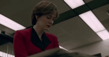 A Woman In A Red Jacket Is Sitting At A Table Reading A Book . GIF