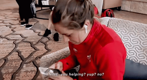 A Woman In A Red Jacket Is Sitting On A Couch Looking At Her Phone And Says " Janine You Helping " GIF