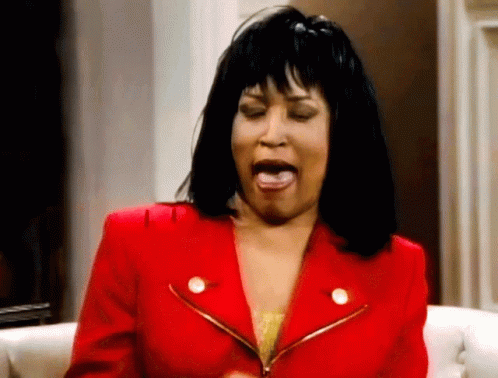 A Woman In A Red Jacket Is Sitting On A Couch With Her Mouth Open GIF