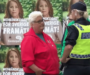A Woman In A Red Jacket Is Standing In Front Of A Poster That Says " Medmannenslighet For Sverige Framat " GIF