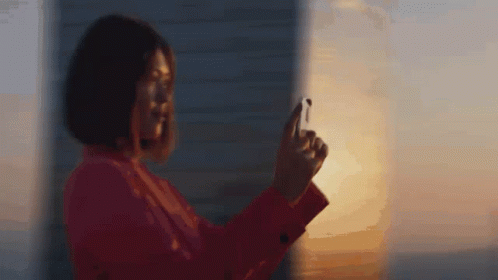 A Woman In A Red Jacket Is Taking A Picture Of The Sunset With Her Phone GIF