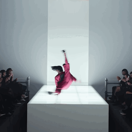 A Woman In A Red Jumpsuit Is Doing A Trick On A White Podium GIF