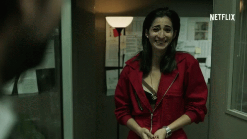 A Woman In A Red Jumpsuit Is Smiling In Front Of A Netflix Sign GIF